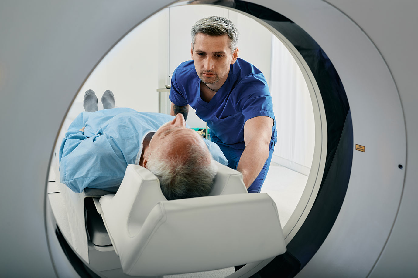 Male in scrubs sliding patient into imaging machine.